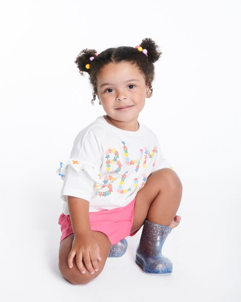 Child model in pink shorts and white shirt wearing a pair of blue glitter Welly baby rain boots
