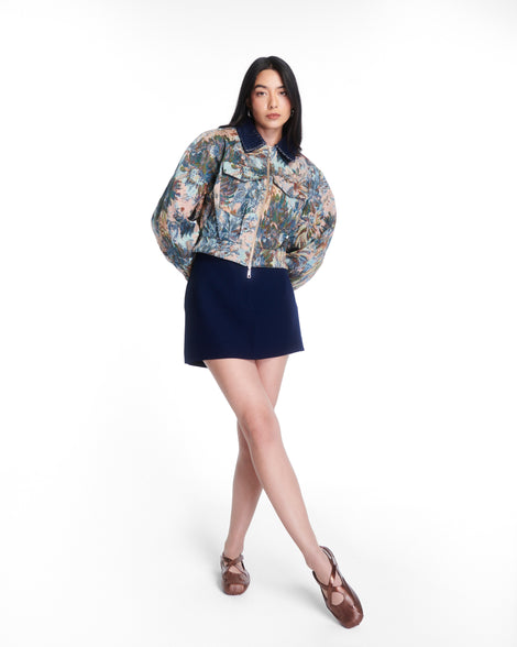 Model in a black skirt and multicolored jacket wearing a pair of bronze Aira flats with top straps