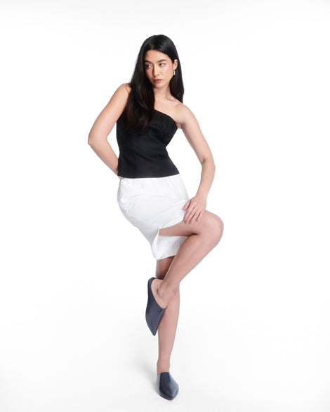 Model in a black top and white skirt wearing a pair of grey She slip ons with pointed toe