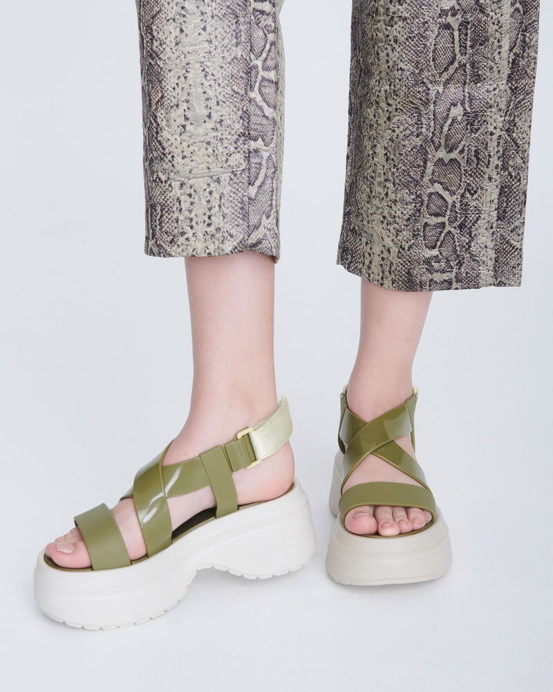 Model's legs wearing a pair of beige Stand platform sandals with army green straps