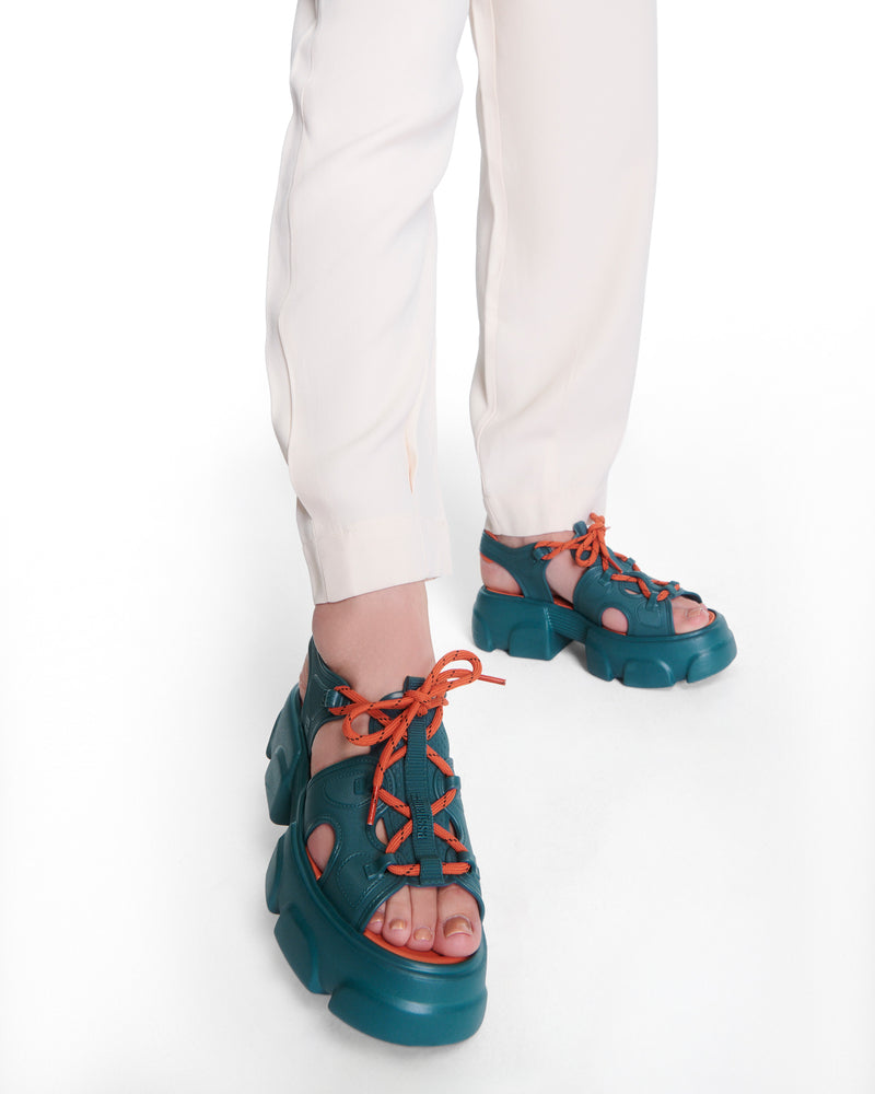 Model's legs wearing a pair of blue Camp platform sandals with orange laces and accents