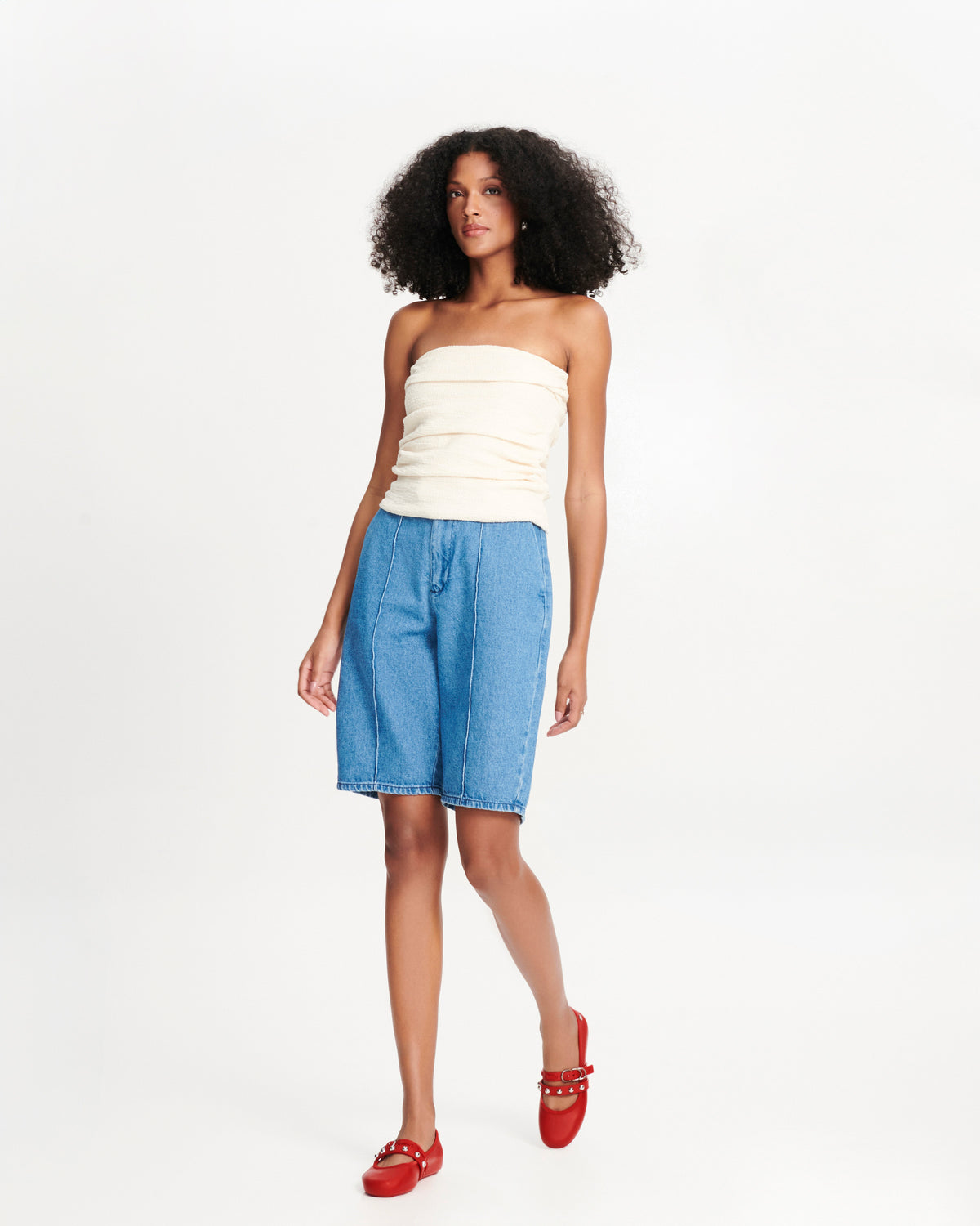 Model in a white top and long jean shorts wearing a pair of red Soft Ballerina Studs flats with silver embellishments