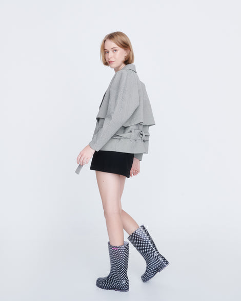 Model in a black skirts and grey jacket wearing a pair of black with white polka dots Welly rain boots