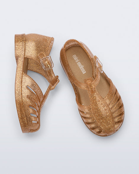 Side and top view of a pair of glitter gold Aranha 79 baby flats with buckle
