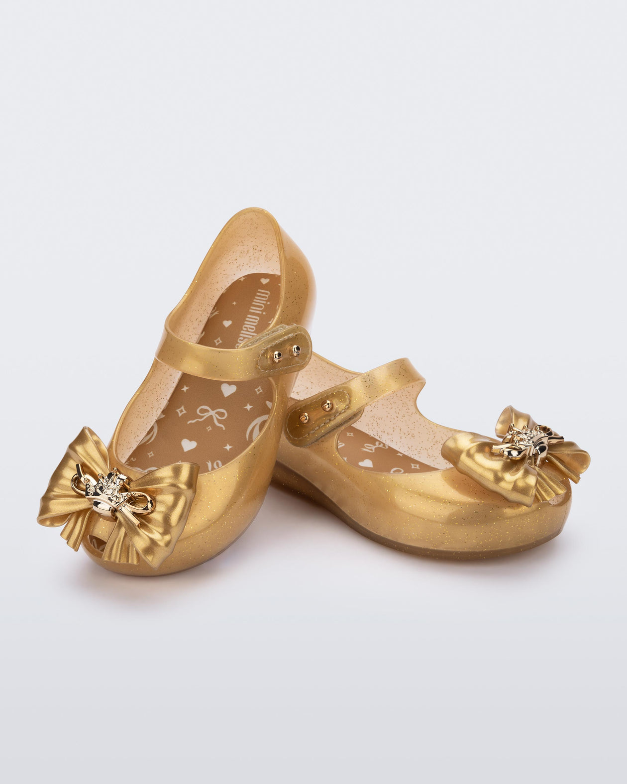 Angled view of a pair of glitter gold Ultragirl Princess ballerina baby flats with bow on top and silver details