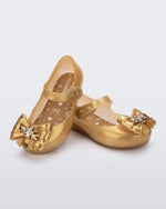 Angled view of a pair of glitter gold Ultragirl Princess ballerina baby flats with bow on top and silver details