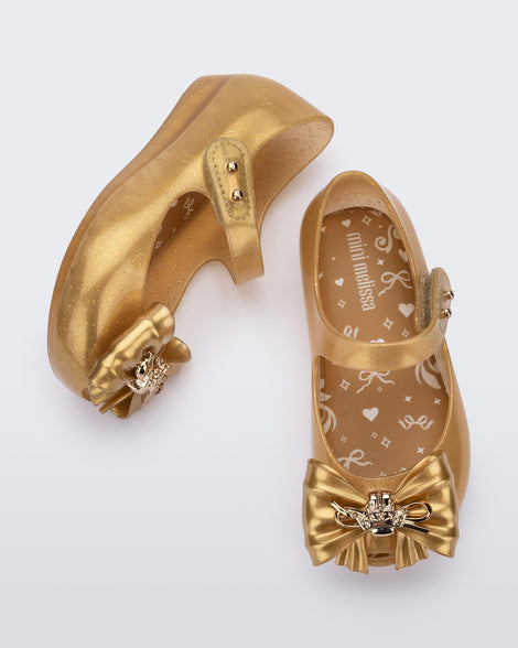 Top and side view of a pair of glitter gold Ultragirl Princess ballerina baby flats with bow on top and silver details