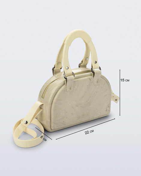 Angled view of a beige Bowling bag with handle strap and cross body strap with bag dimensions of 22cm x 8cm x 15cm