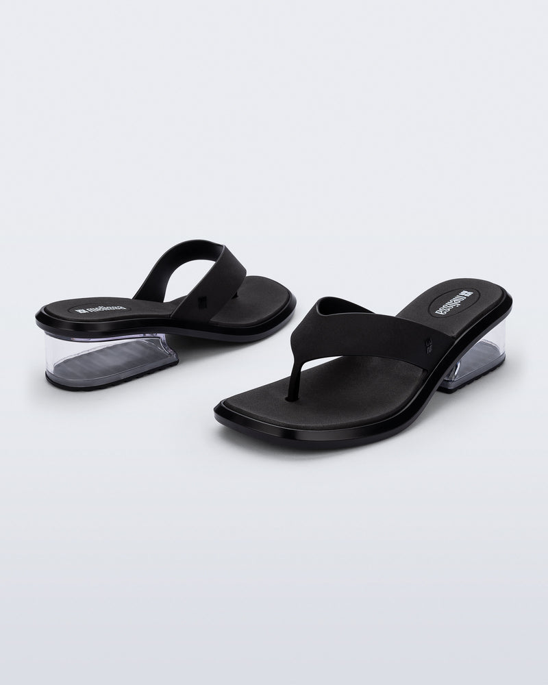 Back and angled view of a pair of black Margot flip flops with clear low heel 