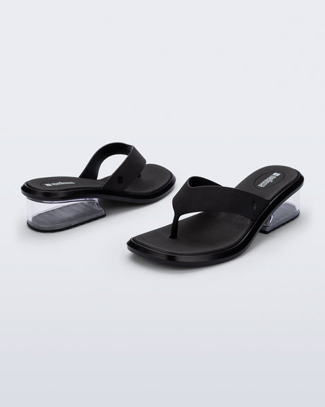 Back and angled view of a pair of black Margot flip flops with clear low heel 
