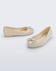 Side and angled view of a pair of beige Sweet Love Chrome kids flats with metallic gold bow