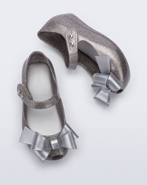 Top and side view of a pair of silver glitter Ultragirl Classy baby flats with silver bow