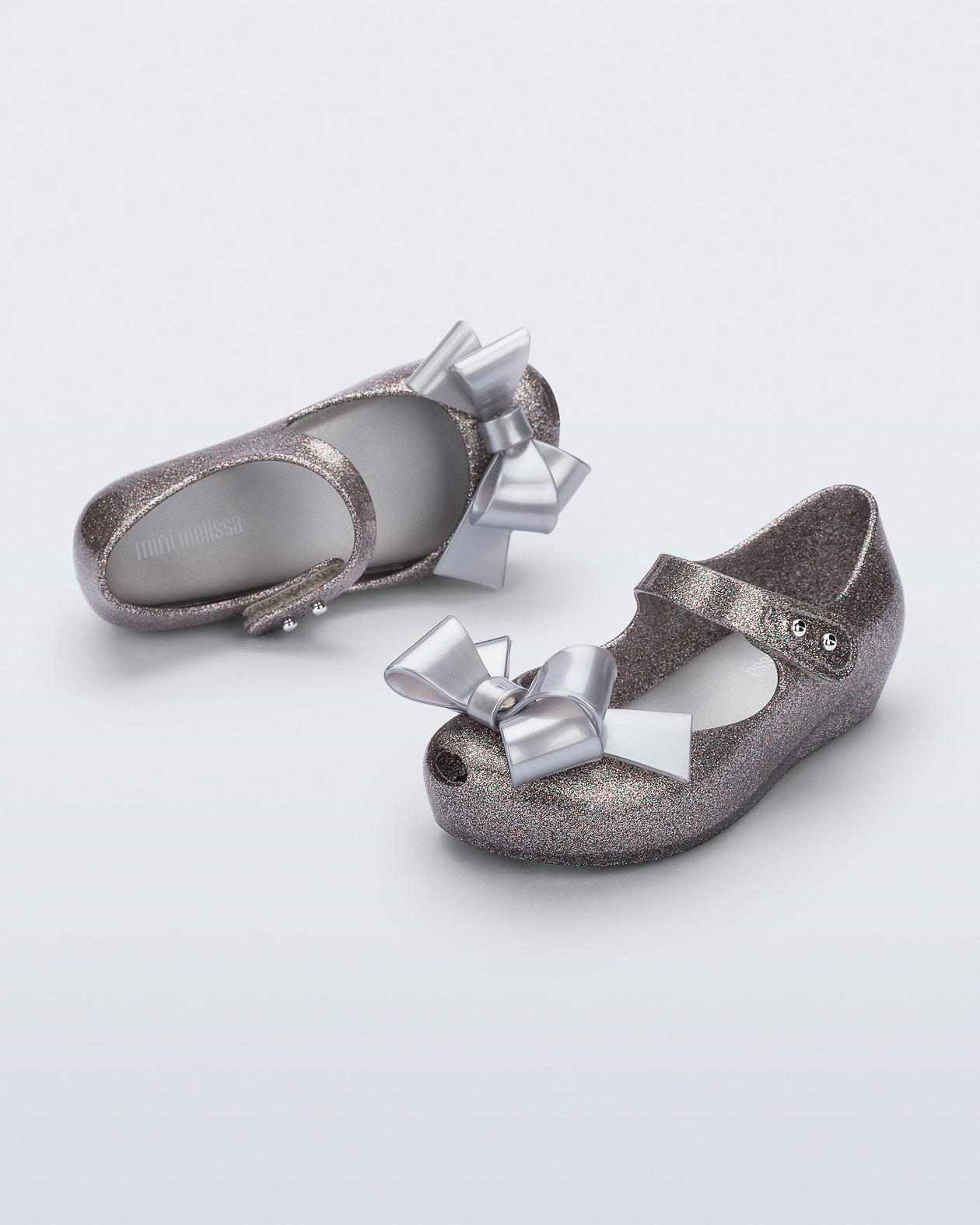 Top and angled view of a pair of silver glitter Ultragirl Classy baby flats with silver bow