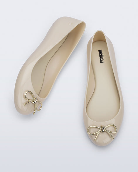 Top and angled view of a pair of beige Sweet Love Chrome flats with gold bow