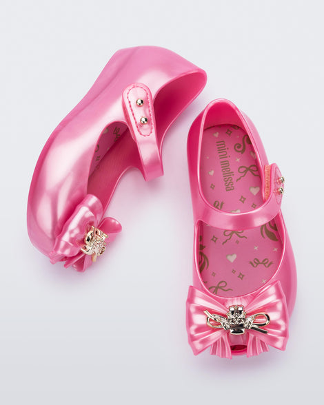 Top and side view of a pair of pearly pink Ultragirl Princess ballerina baby flats with bow on top and silver details