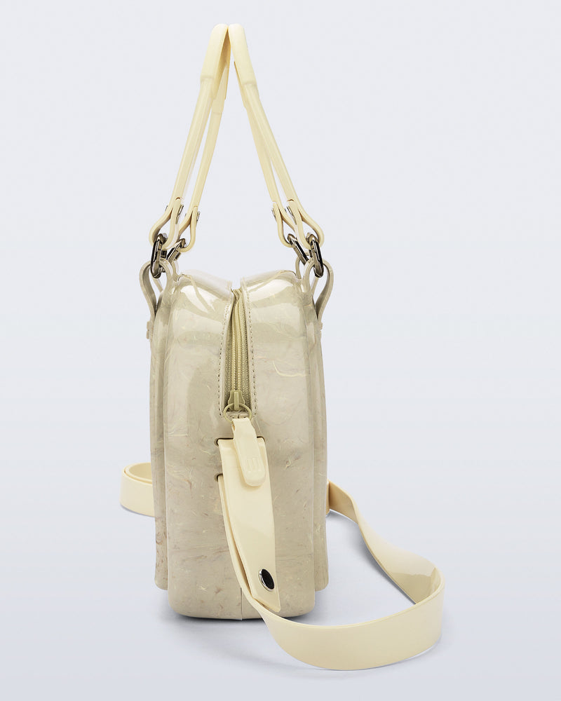 Side view of a beige Bowling bag with handle strap and cross body strap