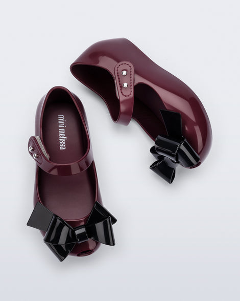 Top and side view of a pair of burgundy Ultragirl Classy baby flats with black bow