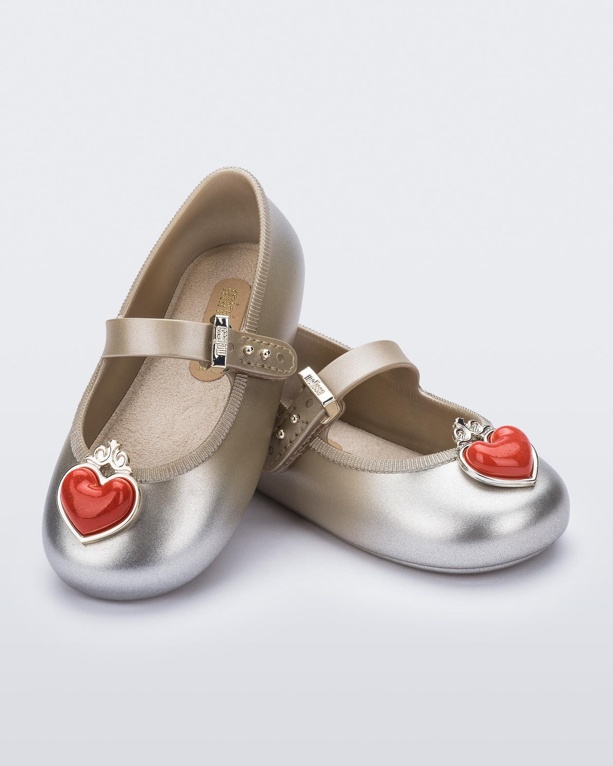 Angled view of a pair of gold/silver Soft Ballerina Princess baby flats with a red heart on top