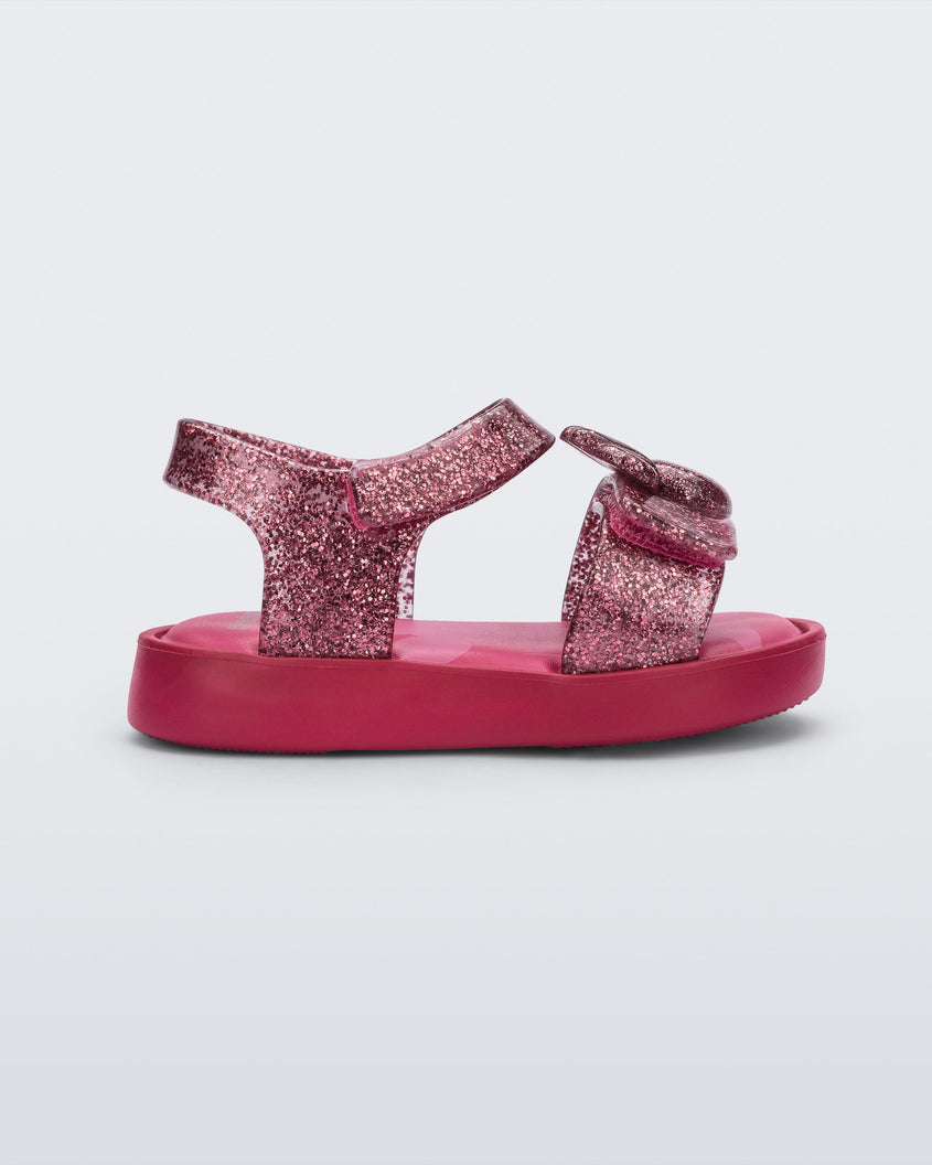 Side view of a glitter pink Mini Melissa Jump sandal with a Mickey Mouse logo detail on the front strap and an ankle strap