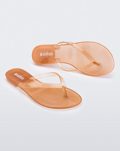 Angled and top view of a pair of clear beige Harmonic Jelly flip flops