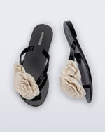 Top and side view of a pair of black Harmonic Petals kids flip flops with beige flowers