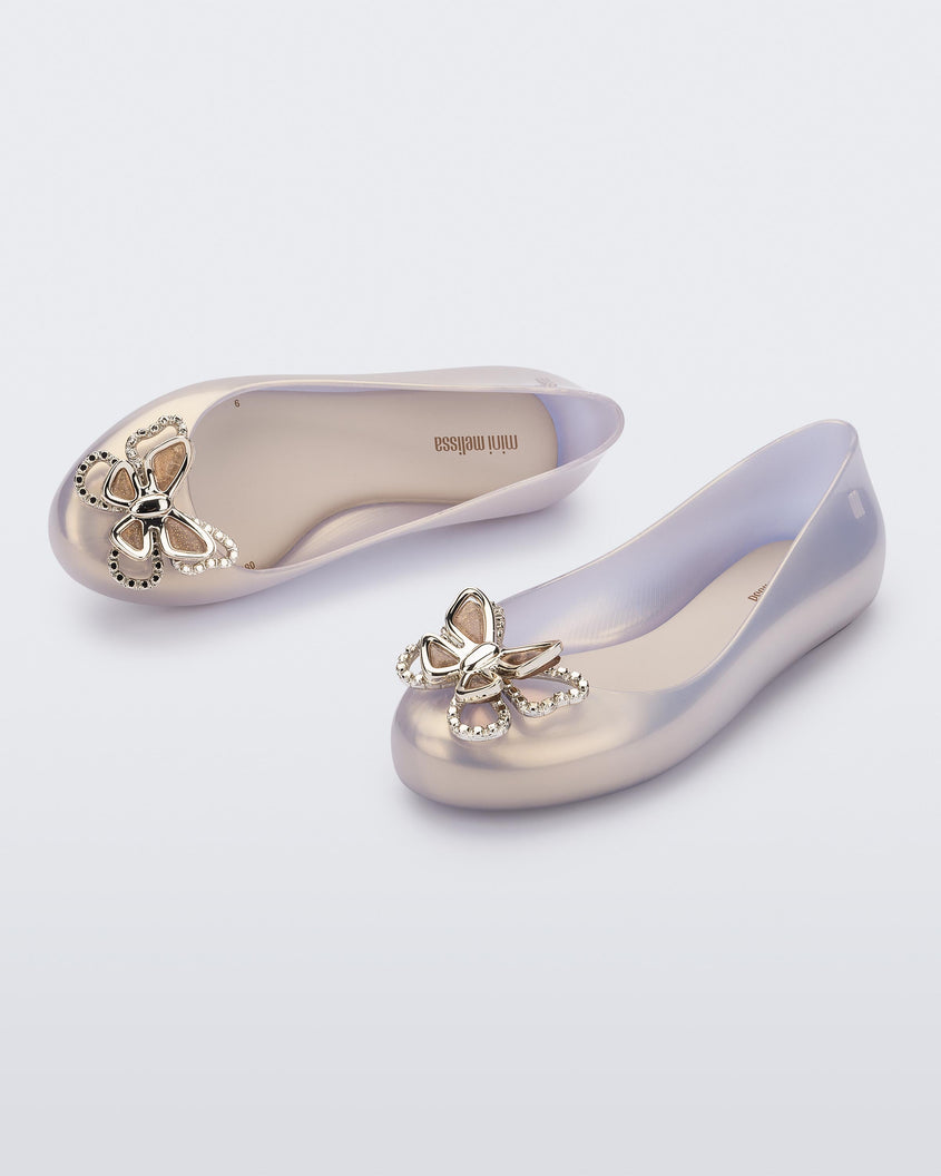 An angled front and top view of a pair of pearly gold Mini Melissa Sweet Love Butterfly flats with a gold butterfly detail on the toe