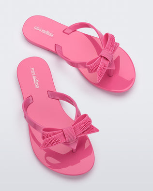Top view of a pair pink Harmonic M Lover kids flip flops with Melissa logo on bow