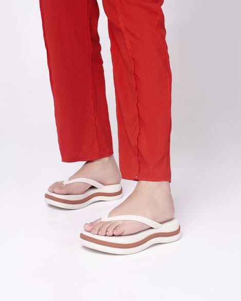 A model's legs in red pants, wearing a pair of beige/brown Melissa Leblon platform flip flops with details that mimic sisal braids on the sole and strap