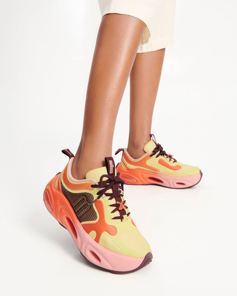 Model's legs wearing a pair of orange/green/pink X Loop sneakers