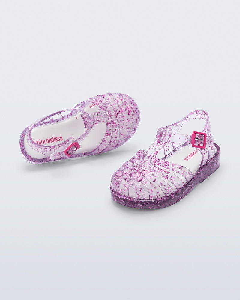 Top and angled view of a pair of clear Possession Elements baby sandal with pink glitter hearts