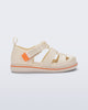 Side view of a beige Smash closed toe baby sandal with orange trim