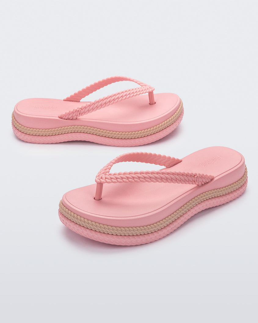 An angled front and side view of a pair of pink/beige Melissa Leblon platform flip flops with details that mimic sisal braids on the sole and strap
