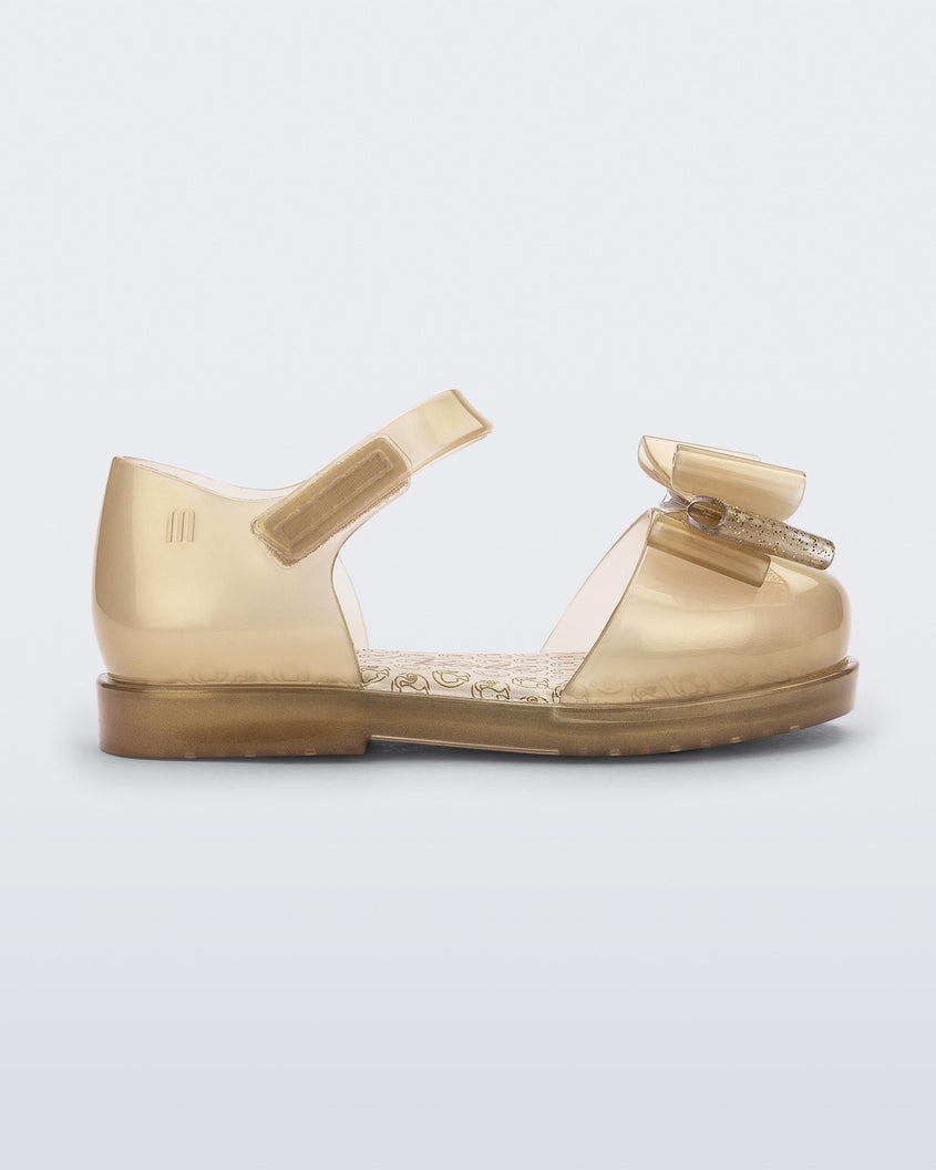 Side view of a pearly beige Mini Melissa sandal with a Barbie bow detail on the front toe, pearly beige ankle strap and a Barbie logo sole