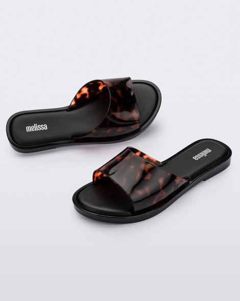 An angled side and top view of a pair of black tortoiseshell Melissa Miranda slides
