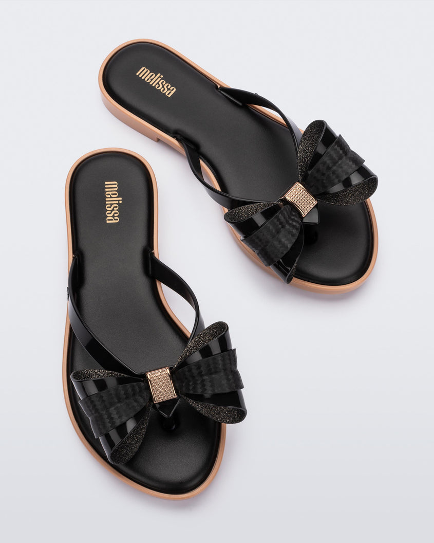 Overhead view of a pair of Melissa slim strap flip flops in black with bow applique