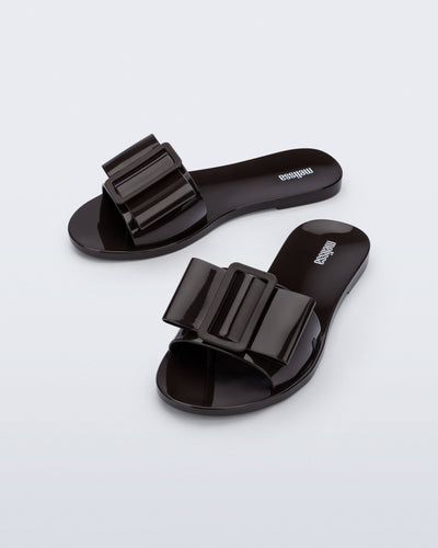 Angled view a pair of brown Babe slide sandals with large bow on top.