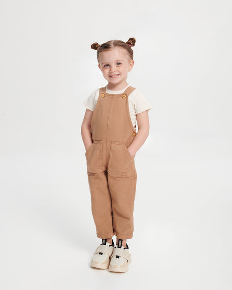 Child model in brown overalls wearing a pair of off white X Beat baby sneakers with black trim