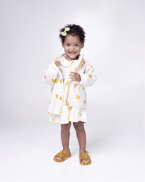 Toddler model in a white with yellow dots dress wearing a pair of yellow Free Cute baby sandals with leopard print.
