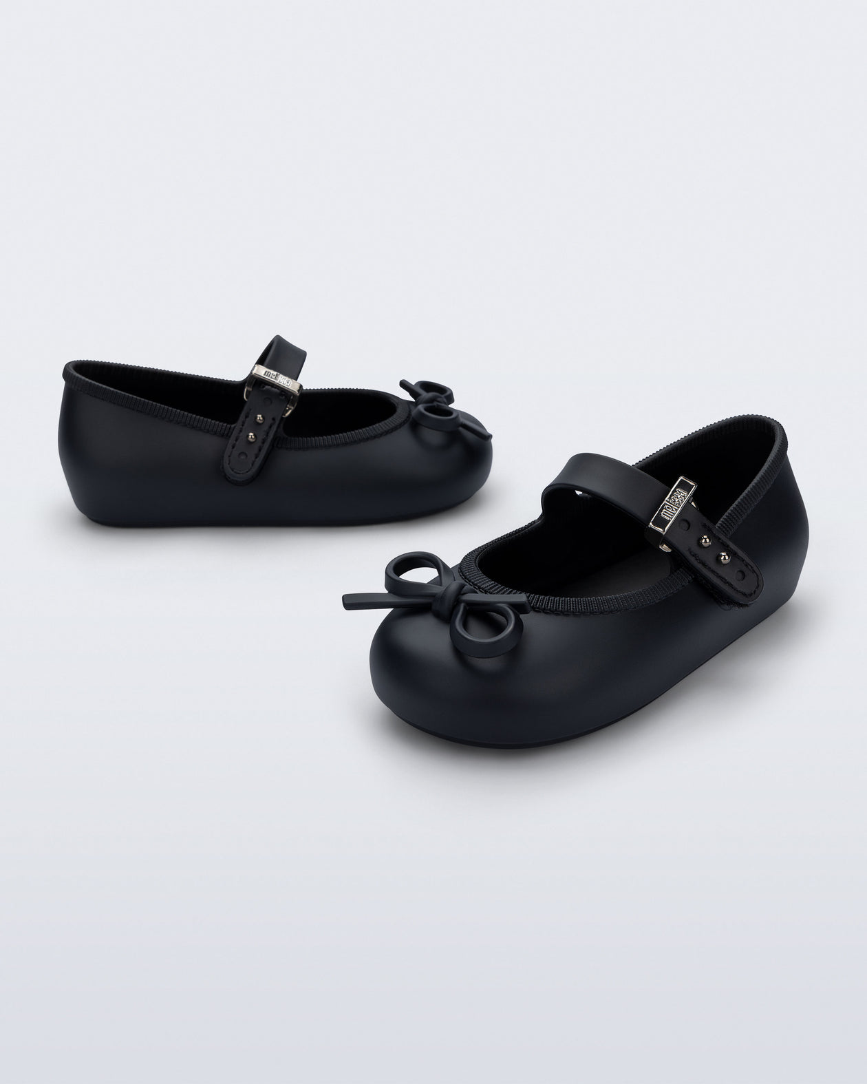 Side and angled view of a pair of black Soft Ballerina Delicate Bow baby flats with top strap and bow