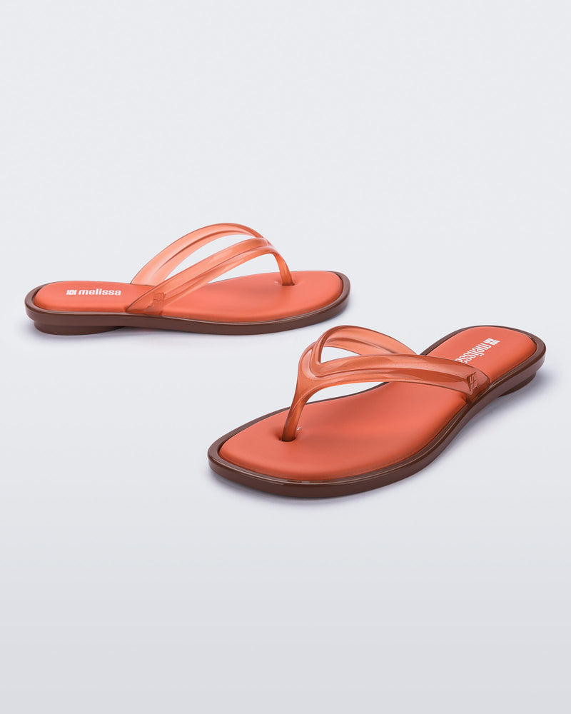 Side and angled view of a pair of orange Wave Flip Flops with small heel and brown sole