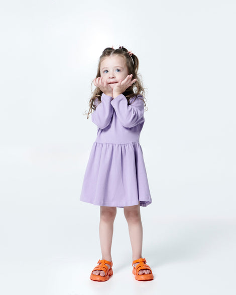 Model in a lilac dress wearing a pair of orange Ella baby sandals