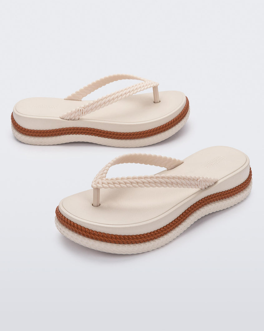 An angled front and side view of a pair of beige/brown Melissa Leblon platform flip flops with details that mimic sisal braids on the sole and strap
