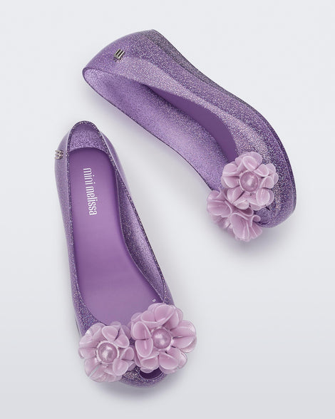 Side and top view of a pair clear glitter purple Ultragirl Springtime kids flat with two purple flowers and peep toe.