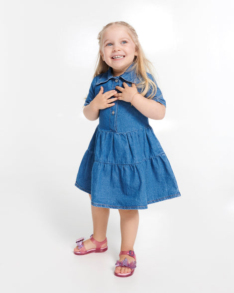 Child model in a blue dress wearing a pair of glitter pink baby Butterfly sandals with butterflies