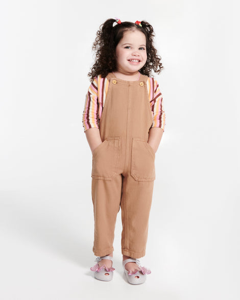 Child model in brown overalls wearing a pair of pearly white Ultragirl Butterfly baby flats with pink butterflies on top