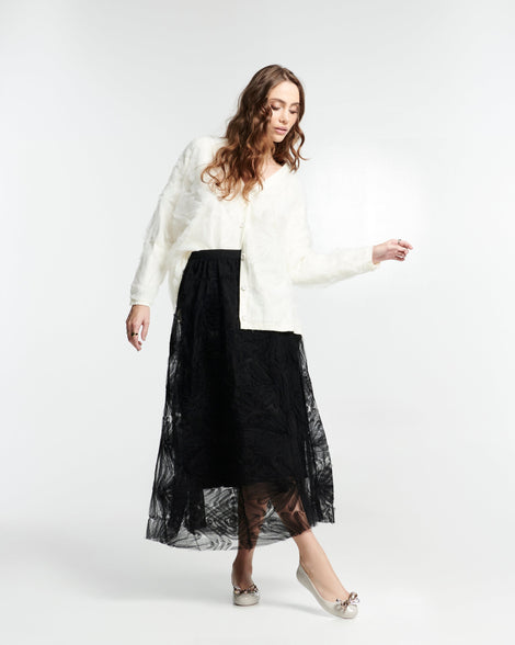 Model in a black skirt and white top wearing a pair of beige Sweet Love Glam ballerina flats with chrome bow