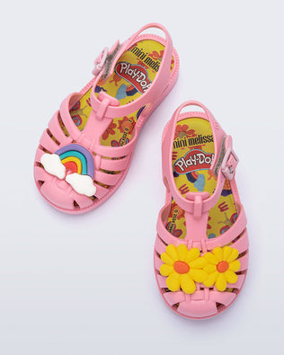 Top view of a matte pink baby Possession + Play Doh sandal with one shoe having a daisy and the other a rainbow on the upper
