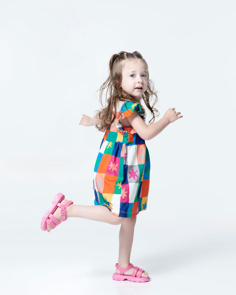 Model in a multicolored dress wearing a pair of pink Ella baby sandals