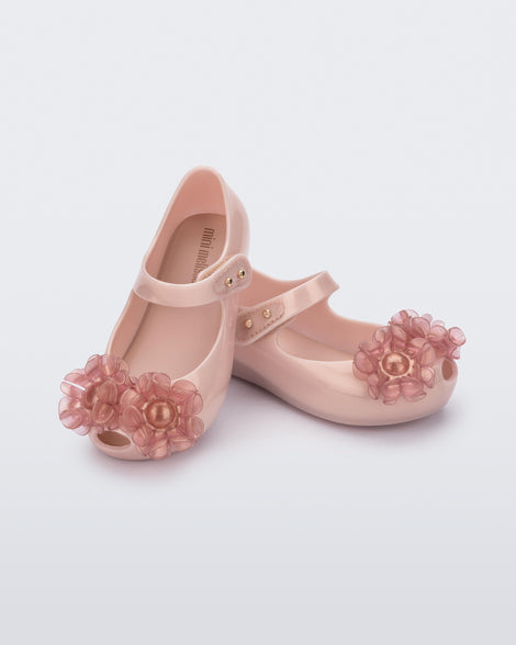 Angled view of a pair of pearly pink Ultragirl Springtime baby flat with two clear pink flowers and peep toe.