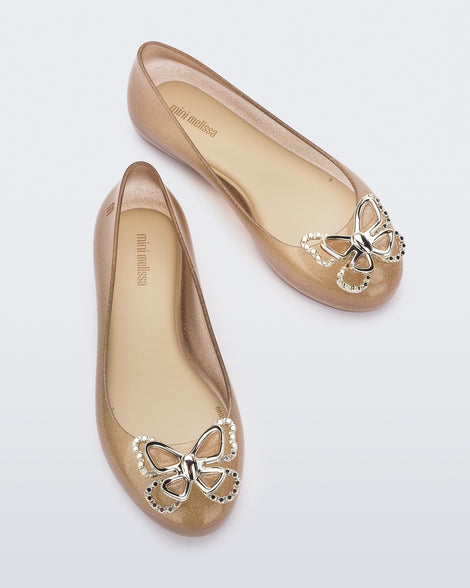 Top view of a pair of glitter beige Mini Melissa Sweet Love Butterfly flats with a gold butterfly detail on the toe